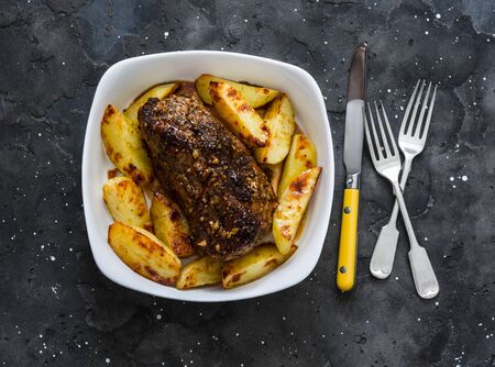Roasted pork fillet with potatoes and spices - delicious simple lunch on a dark background, top viewの写真素材