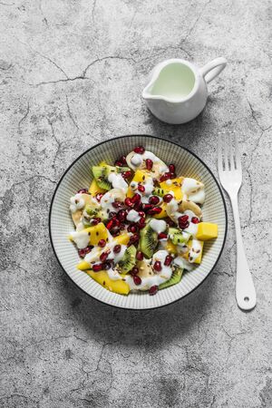 Coconut yogurt and tropical fruit salad for breakfast, snack, dessert. Salad with greek yogurt, banana, mango, kiwi, pomegranate seeds and flaxseeds on a gray background. the view from the topの写真素材