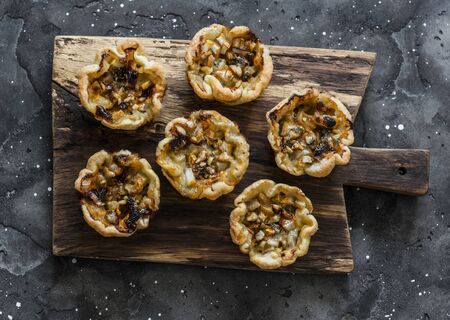 Gorgonzola, pears, honey, walnuts mini quiche on a wooden chopping board, top view on a dark background. Delicious appetizer, dessert, tapasの写真素材