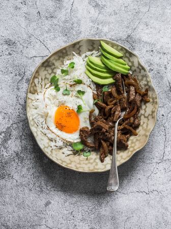 Spicy fried beef, rice, fried egg and avocado - delicious asian style lunch on a grey background, top viewの写真素材