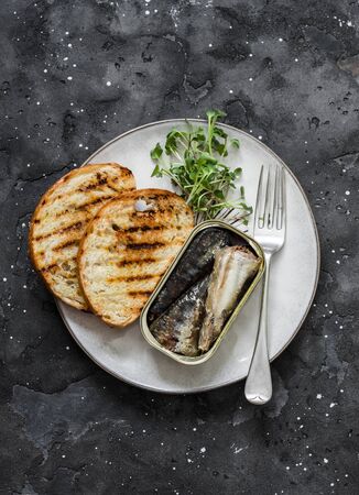 Grilled bread, canned sardines, micro greens on a dark background, top view. Delicious breakfast, tapas, appetizersの写真素材