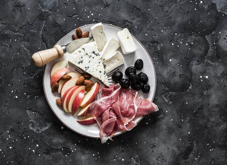 Appetizer plate - prosciutto, gorgonzola, brie cheese, olives, apples, nuts almonds on a dark background, top viewの写真素材