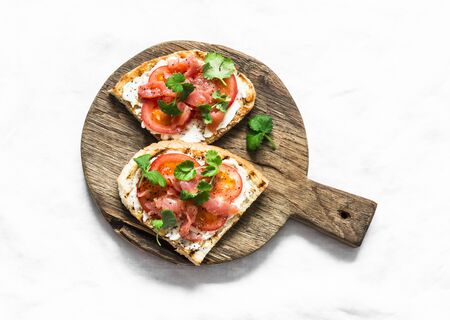 Smoked salmon, tomatoes, cream cheese, cilantro sandwich on a rustic cutting board on a light background, top viewの写真素材