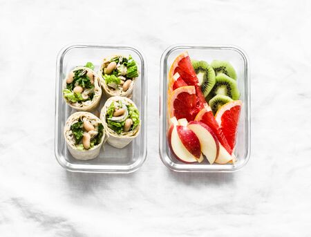 Healthy food lunch box - fresh fruit and chicken, beans, green salad pita bread wraps on a light background, top view. Sweet and savory lunch boxの写真素材