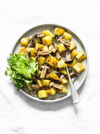 Fried potatoes with mushrooms and green salad - delicious simple vegetarian lunch on a light background, top viewの写真素材