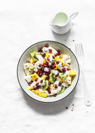Greek yogurt and tropical fruit salad for breakfast, snack, dessert. Salad with greek yogurt, banana, mango, kiwi, pomegranate seeds and flaxseeds on a gray background, top viewの写真素材