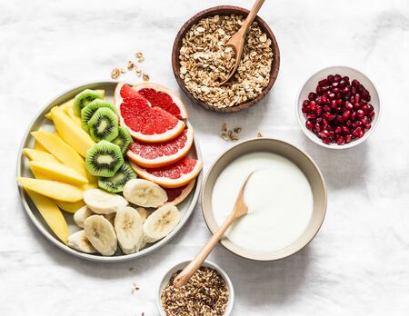 Breakfast set table - fresh tropical fruits, greek yogurt, granola on a light background, top view. Delicious healthy diet food concept. Flat layの写真素材