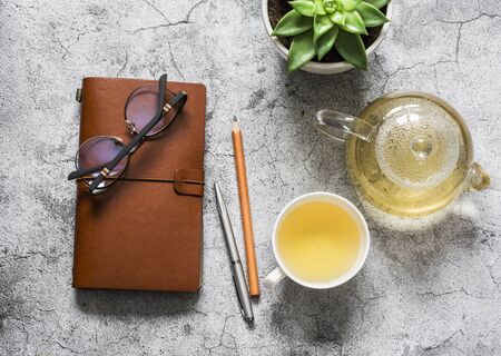 Tea break. Green tea, work desk with leather business organizer, succulent flower on grey background, top viewの写真素材