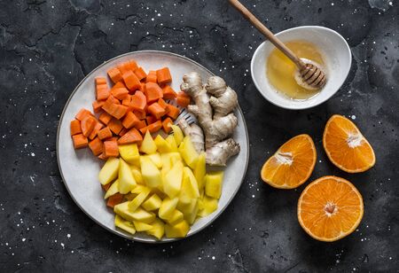 Ingredients for smoothies - fresh ripe mango, carrot, orange, honey, ginger on a dark background, top view. Detox drinkの写真素材