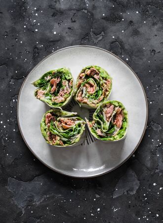 Baked salmon, avocado puree, green  salad tortilla wrapped rolls sandwich on a dark background, top viewの写真素材