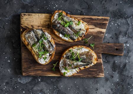 Grilled bread sardines micro greens sandwiches on a rustic cutting board on a dark background, top viewの写真素材