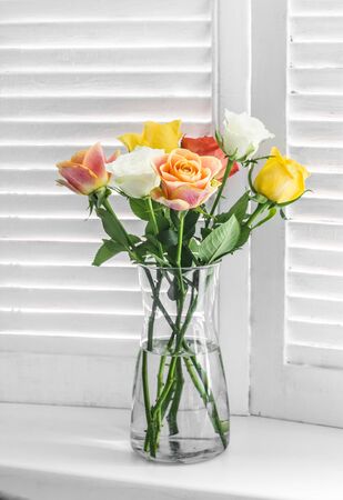 Bouquet with multicolored roses on a window with wooden blinds on a light backgroundの写真素材