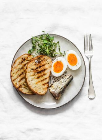 Grilled bread, sardines, boiled eggs, micro greens on a light background, top view. Delicious breakfastの写真素材