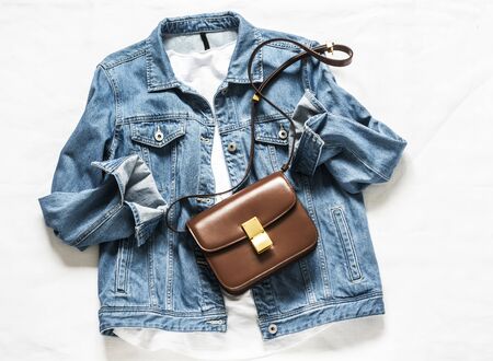 Women 's denim oversize jacket, white cotton t- shirt, cross body brown leather bag on a light background, top view. Fashion style conceptの写真素材