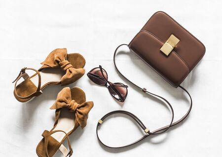Cross body brown leather bag, suede wedge sandals and sunglasses on a light background, top view. Fashion conceptの写真素材