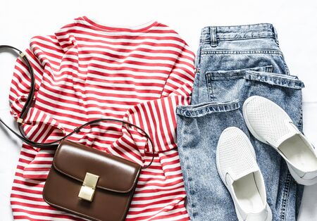 Women's long-sleeve t- shirt with red stripes, blue mom jeans, sneakers and cross body brown leather bag on a light background, top view. Fashion conceptの写真素材