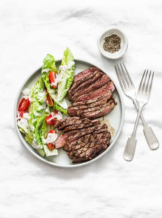 Beef steak and romaine cherry tomatoes yogurt dressing salad on a light background, top viewの写真素材