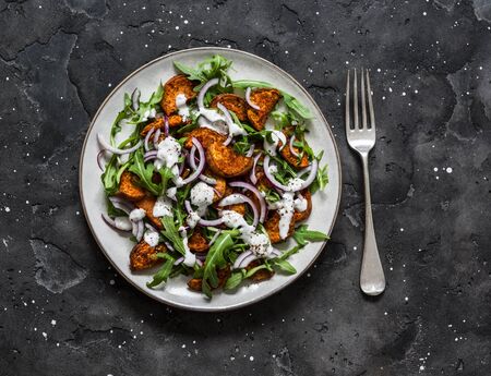 Baked crispy sweet potatoes, arugula, red onion and yogurt mustard dressing salad on a dark background, top viewの写真素材