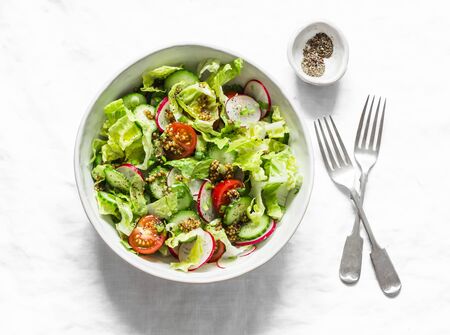 Easy vegetarian vegetable salad with fresh vegetables. Cherry tomatoes , romano lettuce, cucumbers, radishes and french mustard, olive oil, lemon salad dressing on a light background, top view. Diet foodの写真素材