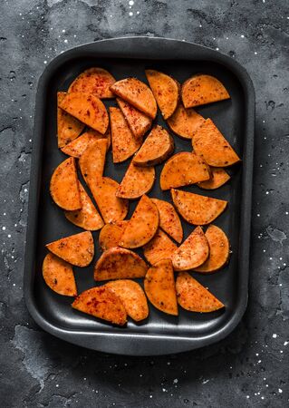 Raw sweet potato slices on a baking tray on a dark background, top view. Cooking baked sweet potatoesの写真素材