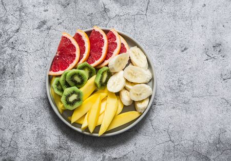 Fresh tropical fruits mango, kiwi, bananas, grapefruits in a plate on a grey background, top view. Delicious healthy dessert, snackの写真素材