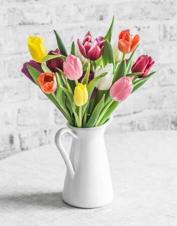 Bouquet of multicolored tulips in a jug on the table in a bright roomの写真素材