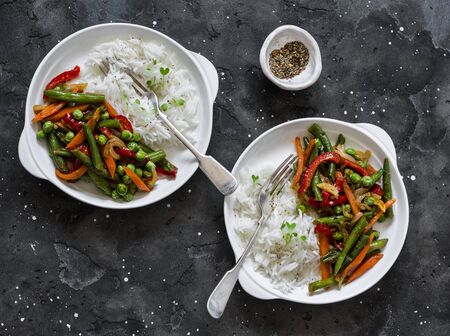 Green beans, sweet peppers, carrots, onions, green peas stir fry and rice on a dark background, top view. Fast diet vegetarian lunchの写真素材