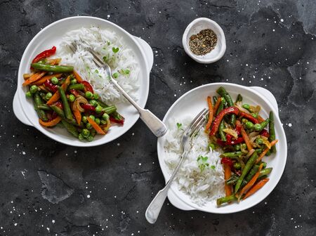 Green beans, sweet peppers, carrots, onions, green peas stir fry and rice on a dark background, top view. Fast diet vegetarian lunch