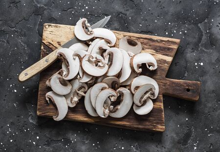Sliced brown mushrooms on a rustic chopping board on a dark background, top view. Food cooking ingredientsの写真素材