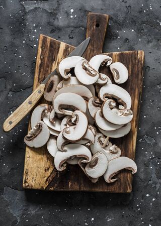 Sliced brown mushrooms on a rustic chopping board on a dark background, top view. Food cooking ingredientsの写真素材