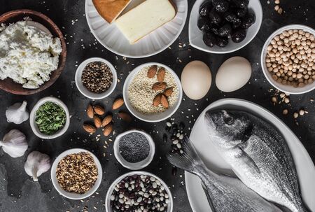 Set of source of calcium in products - fish, sesame, cheese, cottage cheese, poppy seeds, olives, flax seeds, eggs, legumes, almonds, garlic on a dark background, top viewの写真素材