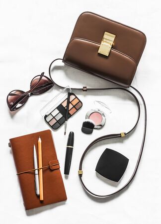 Women's cross body brown leather bag, business organizer, cosmetics and sunglasses on a light background, top view. Fashion beauty conceptの写真素材