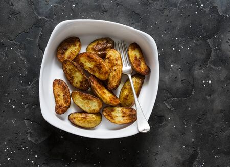 Roasted new potatoes in baking dish on a dark background, top view. Delicious snack, tapasの写真素材