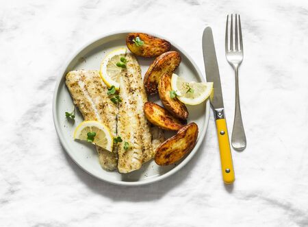 Fish fillet baked with lemon and new potatoes on a light background, top view. Delicious homemade lunchの写真素材