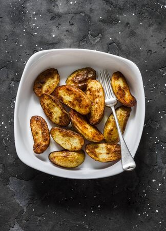 Roasted new potatoes in baking dish on a dark background, top view. Delicious snack, tapasの写真素材