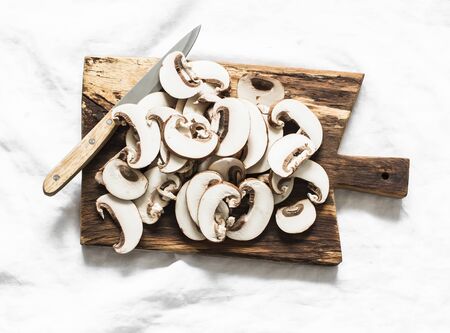 Sliced brown mushrooms on a rustic chopping board on a light background, top view. Food cooking ingredientsの写真素材