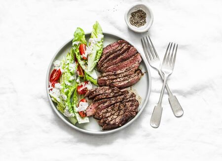 Medium rare beef steak and romaine cherry tomatoes yogurt dressing salad on a light background, top view.Delicious balanced foodの写真素材