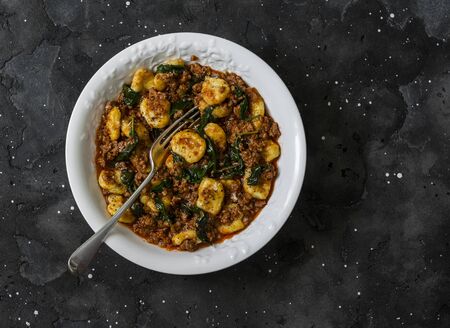 Potato gnocchi with classic bolognese sauce and spinach on a dark background, top viewの写真素材