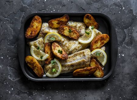 Baked fish fillet and potatoes on a baking sheet on a dark background, top view. Mediterranean style lunchの写真素材
