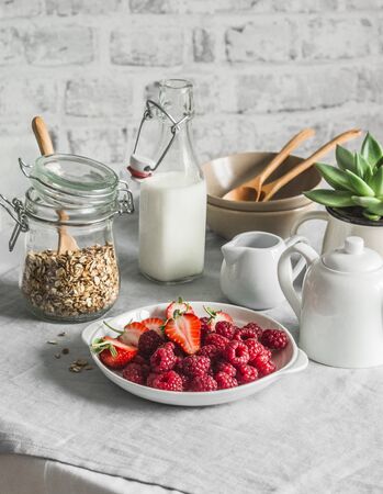 Cozy home breakfast served table - granola, milk, fresh raspberries and strawberries in the light kitchen. Flat layの写真素材