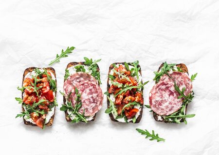 Tomatoes and italian salami sausage rye bread bruschetta on a light background, top view. Copy space. Delicious appetizers for wine, tapasの写真素材