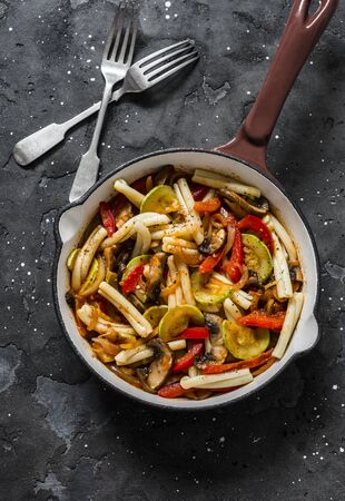 Pasta, zucchini, mushrooms, sweet paprika vegetable stewed tomato sauce in a pan on a dark background, top view. Vegetarian foodの写真素材