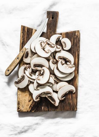 Sliced brown mushrooms on a rustic chopping board on a light background, top view. Food cooking ingredientsの写真素材