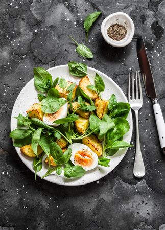 Baked potato, boiled egg and fresh spinach salad on dark background, top view. Delicious breakfast, snackの写真素材