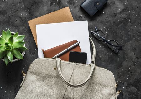 Women's white leather bag with office accessories on a dark background, top view. Business conceptの写真素材