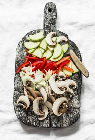 Sliced zucchini, mushrooms, sweet paprika, onions on a rustic chopping board on a light background, top view. Raw food ingredientsの写真素材