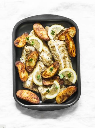 Baked fish fillet and potatoes on a baking sheet on a light background, top view. Mediterranean style lunchの写真素材