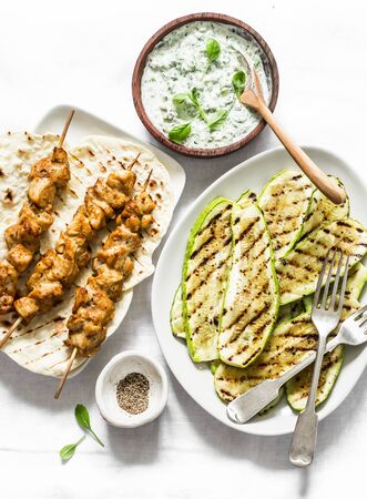Chicken skewers, grilled zucchini, tortillas and tzadziki sauce - delicious greek style lunch on a light background, top viewの写真素材