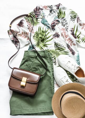 Summer travel, vacation, walking women's clothing - shirt plant print short sleeve, bermuda shorts, sneakers, bag and hat on a light background, top viewの写真素材