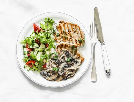 Balanced food - grilled pork with creamy mushroom sauce and fresh vegetable salad on a light background, top viewの写真素材
